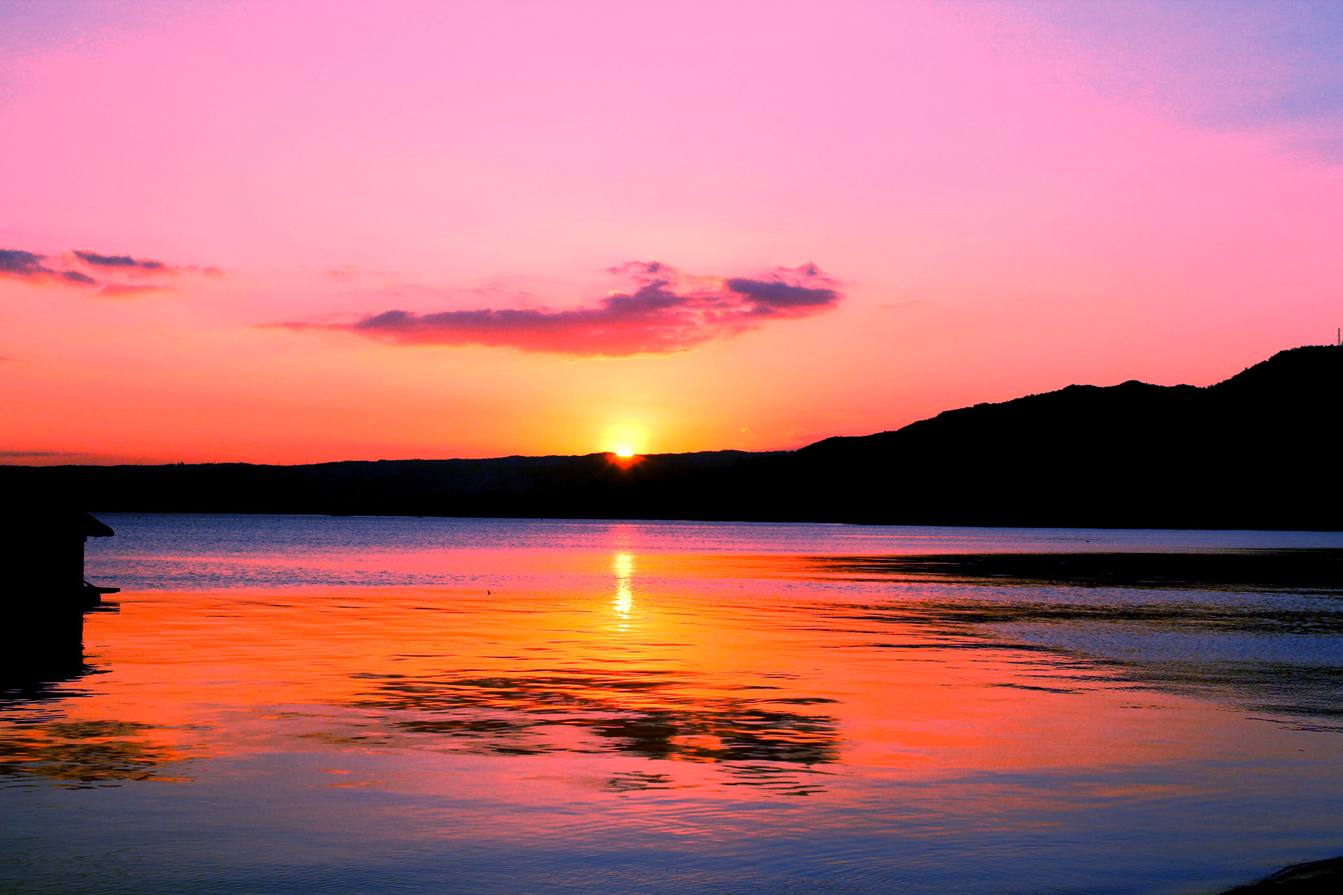 a mountain landscape with a pink sky in the background that reflects over the large body of water in the foreground