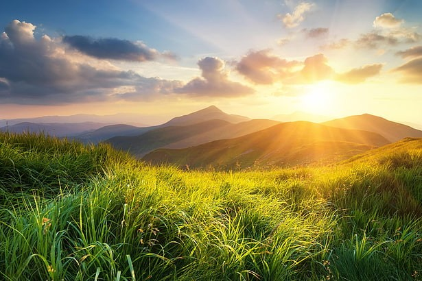 a mountain landscape with a sun peeking out from behind the mountains, and a grassy foreground