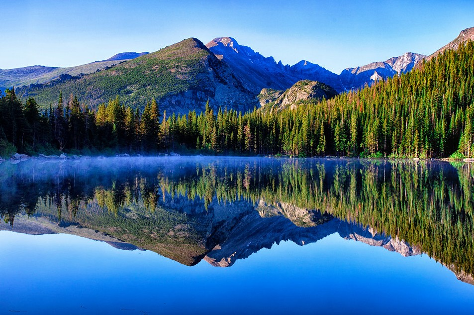 a mountain landscape with a clear blue sky in the background and a body of water with the mountains reflected in the foreground